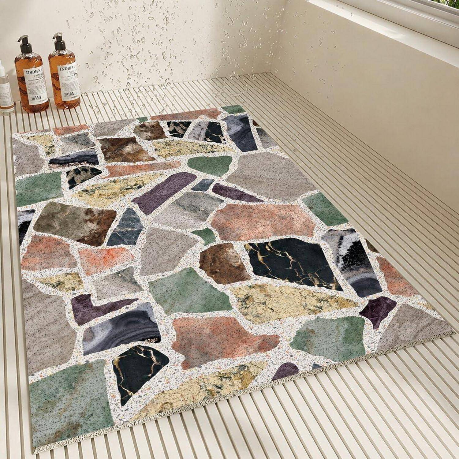 Farbenfroher Mosaikstil-Teppich mit unregelmäßigen steinähnlichen Formen auf einem Badezimmerboden neben zwei bernsteinfarbenen Seifenspendern in der Nähe eines Fensters und eines Waschbeckenbereichs.