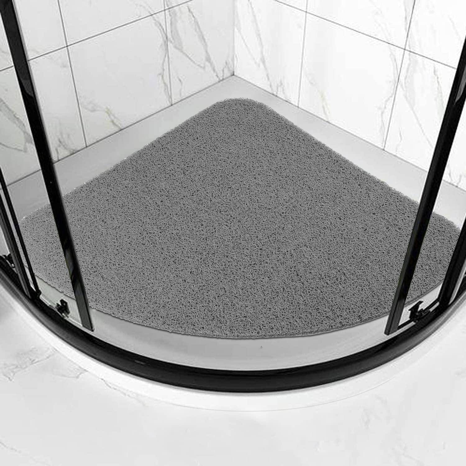 Gekrümmte graue Duschmatte auf dem Boden einer Glasduschabtrennung auf einem weiß gefliesten Badezimmerboden.