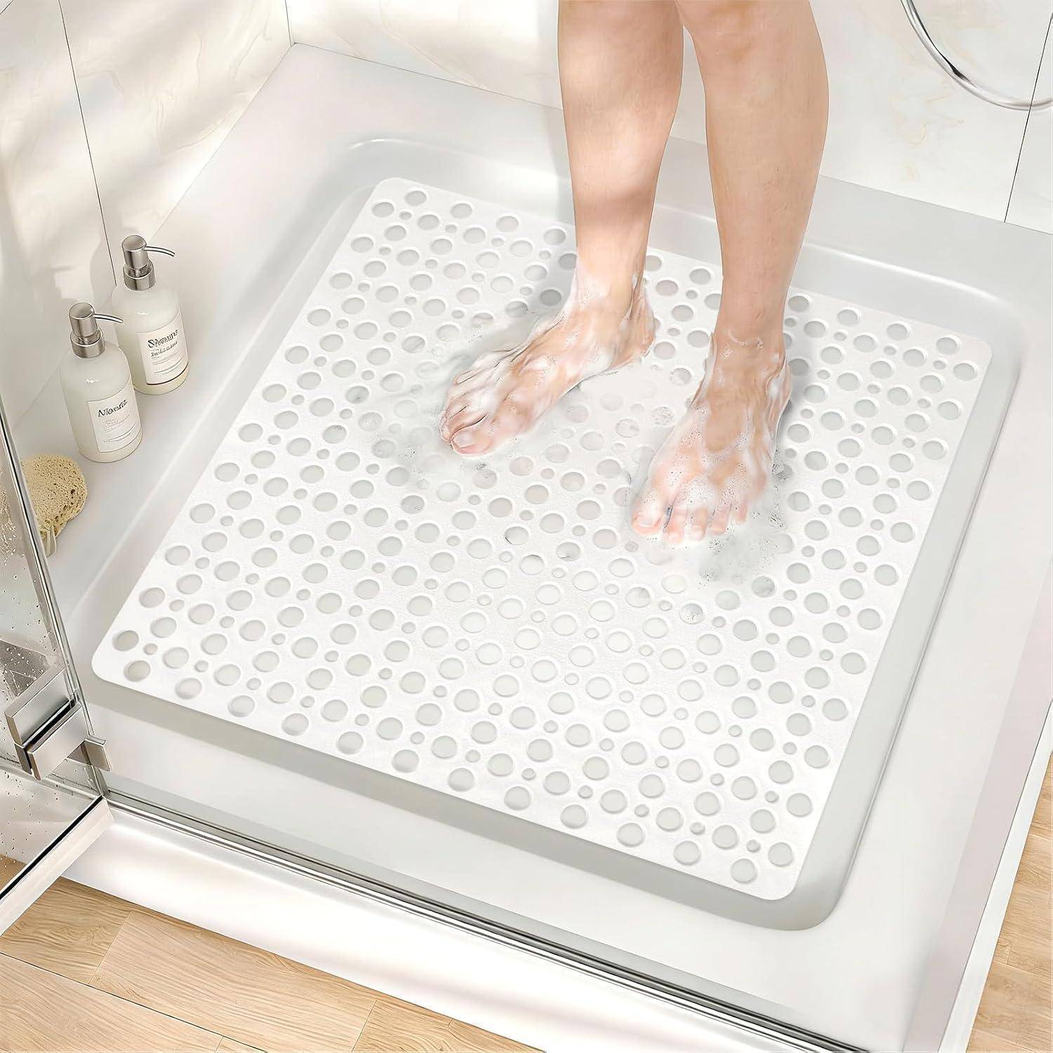 Eine Person steht auf einer weißen strukturierten rutschfesten Badematte in einer begehbaren Dusche und seift ihre Füße unter Wasser ein.