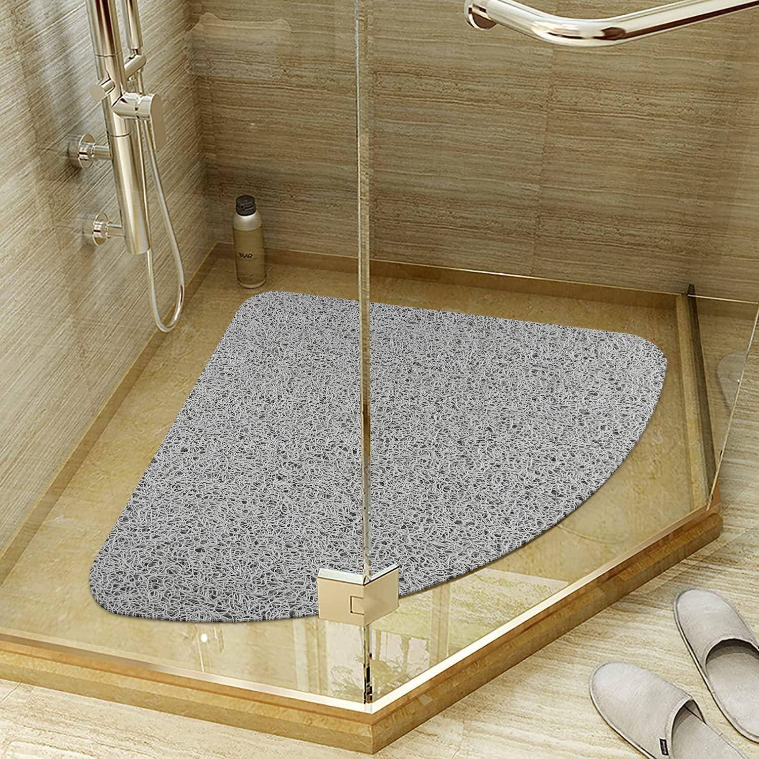Begehbare Dusche mit einer grauen Badmatte auf dem Boden, Glasverkleidung, Handbrausekopf und Hausschuhen außerhalb auf dem Badezimmerboden.