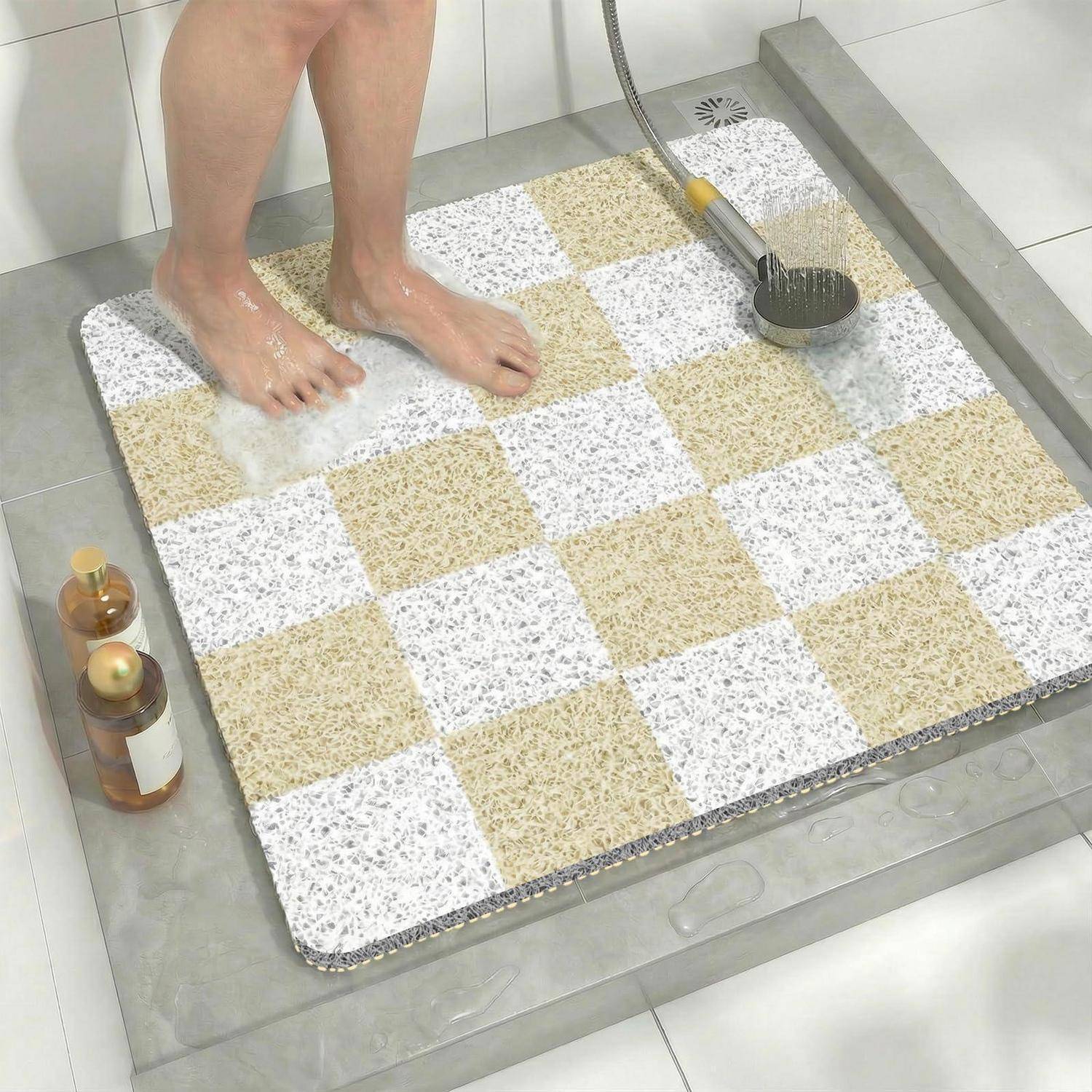 Eine Person wäscht sich die Füße unter der Dusche auf einer karierten rutschfesten Badmatte, mit einer Handbrauseschlauch-Duschkopf und Toilettenartikeln in der Nähe.