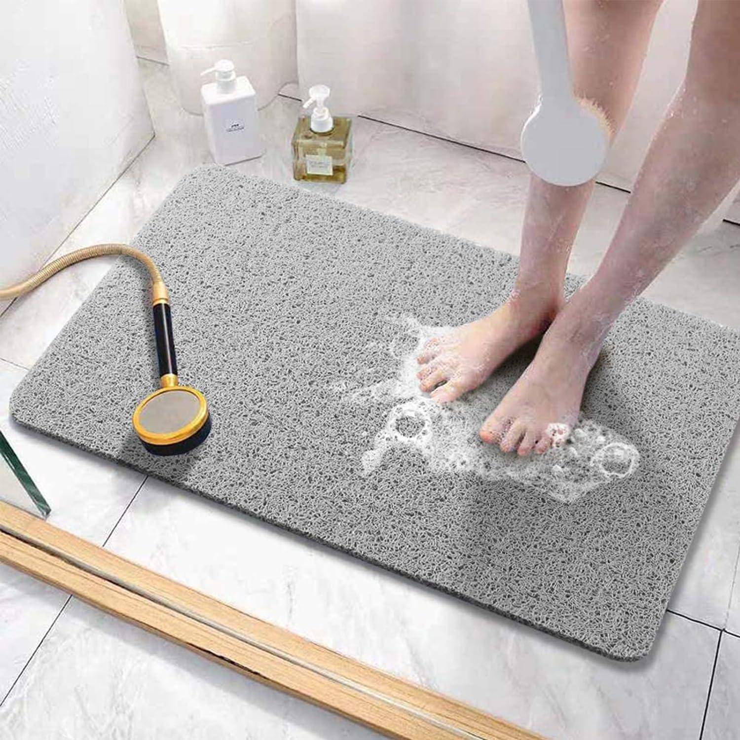 Person duscht auf einer grauen Badmatte, die Wasser aufnimmt, mit einer Handbrause und Toilettenartikeln in der Nähe.