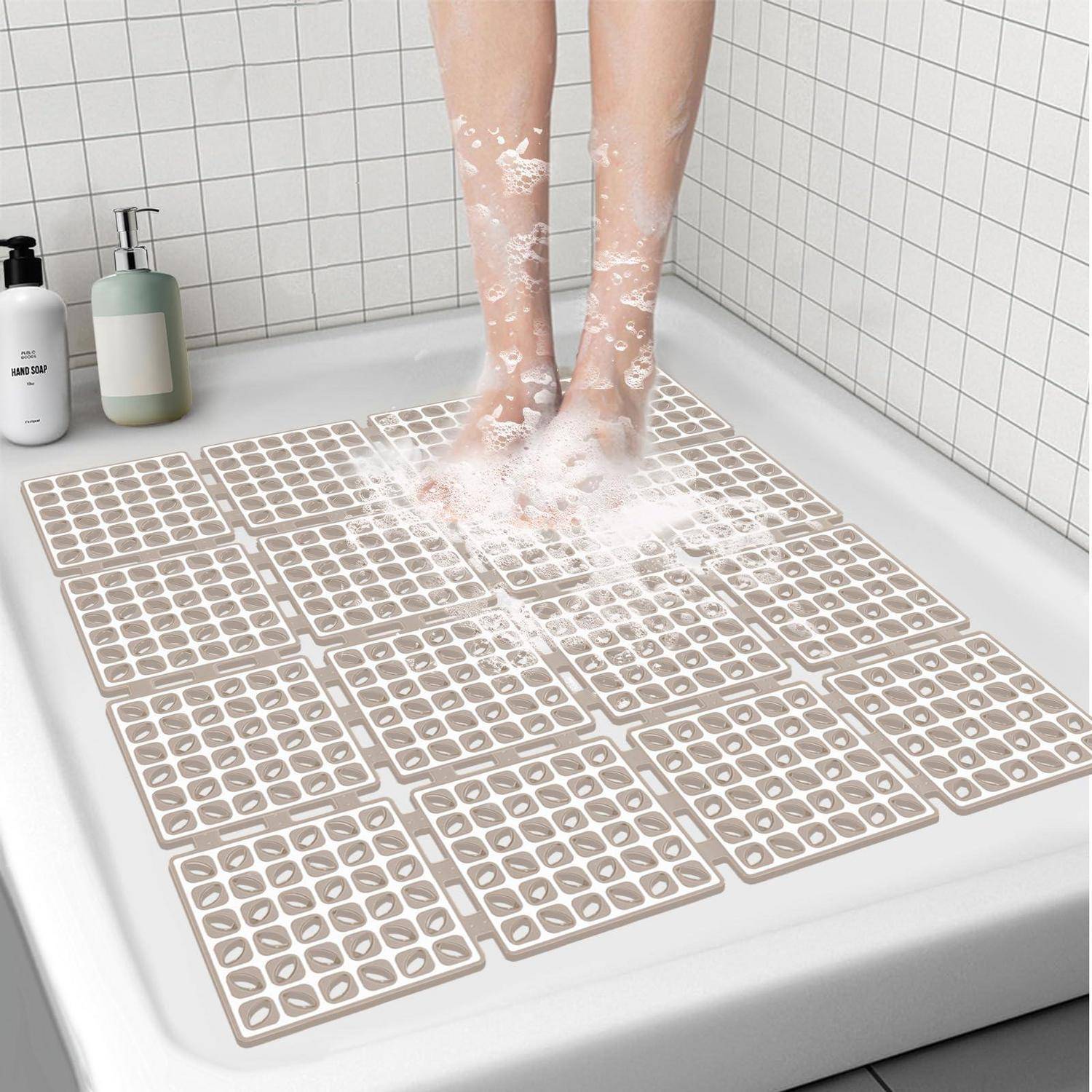 Person, die ihre Füße in einer Dusche mit beigen rutschfesten Badematten, die den Boden bedecken, schrubbt.