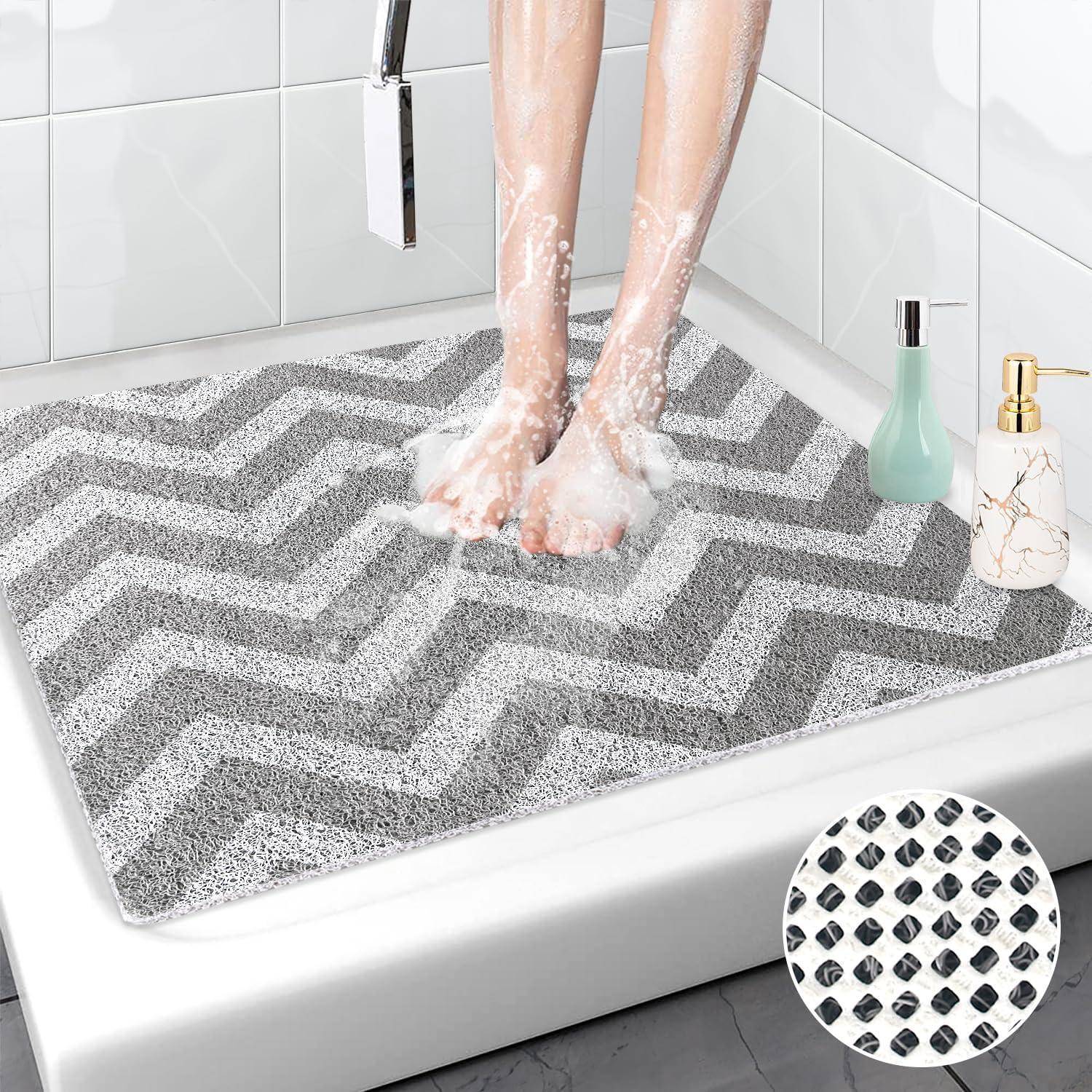 Füße, die auf einer grauen Chevron-Badematte in einer Dusche stehen, mit Seifenschaum; die Einfügung zeigt die strukturierte rutschfeste Rückseite der Matte.