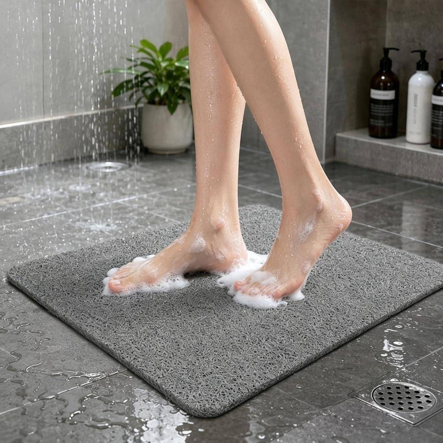 Nackte Füße mit Seifenschaum, die auf einer grauen strukturierten Badematte in einem nassen Duschbereich stehen, mit fließendem Wasser und Toilettenartikeln im Hintergrund.