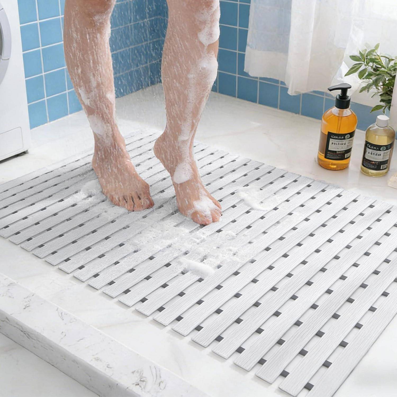 Nackte Beine mit Seife bedeckt, stehen auf einer weißen Lamellenbadematte in einem gekachelten Duschbereich, mit zwei Pumpflaschen in der Nähe.