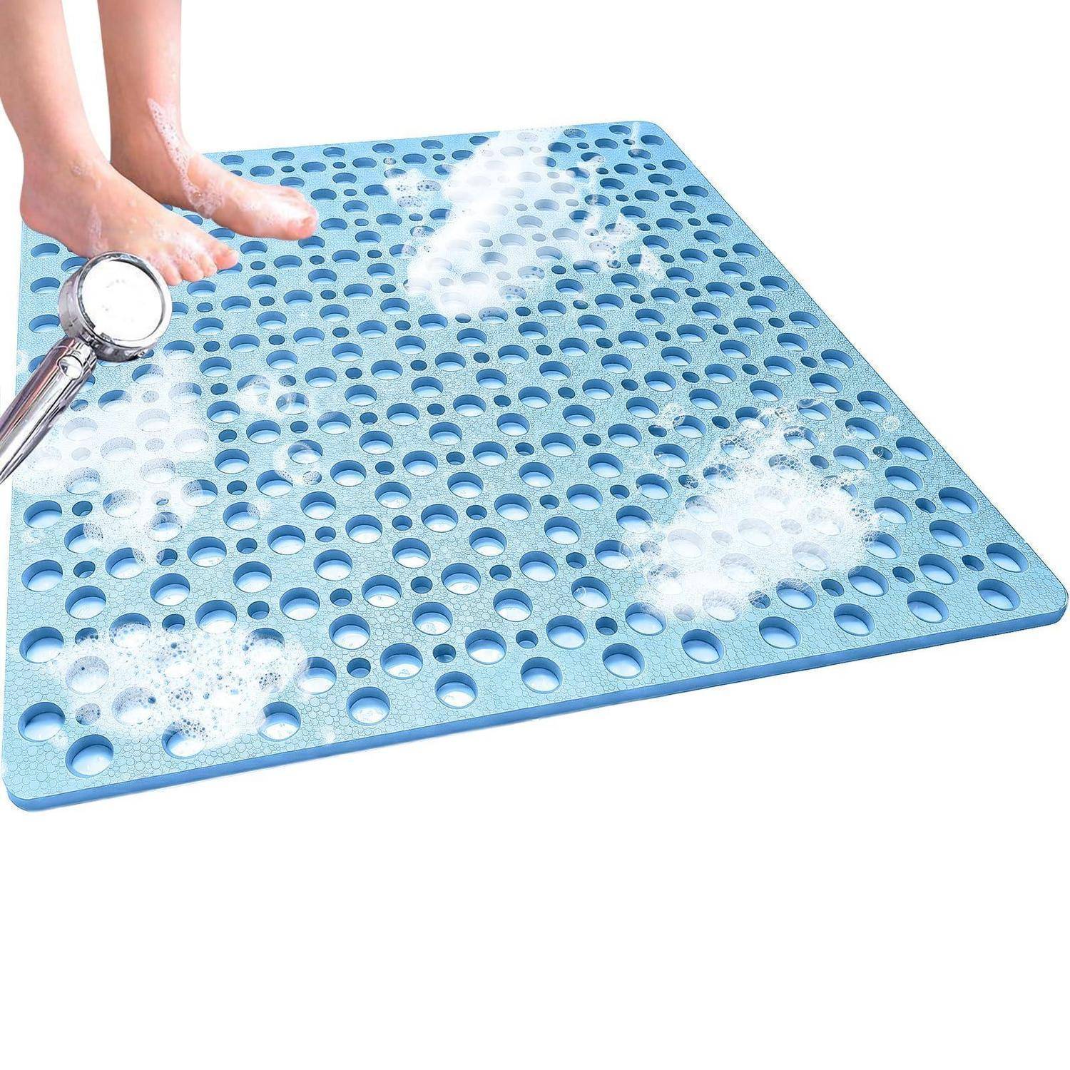 Füße, die auf einer blauen Gummibadematte mit Ablöchern stehen, während Wasser darüber spritzt, zeigt eine rutschfeste Duschenmatte.
