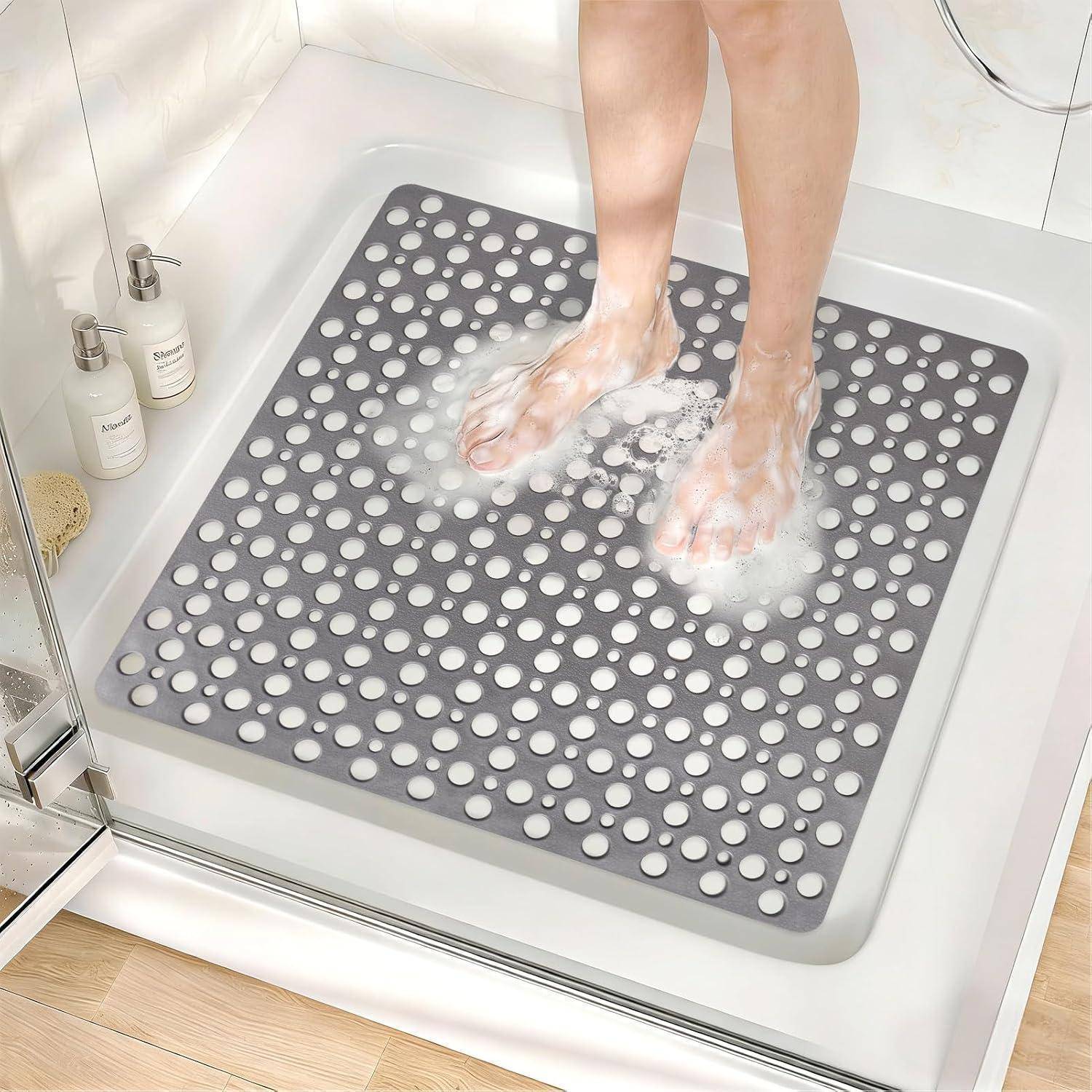 Person wäscht sich die Füße auf einer grauen, perforierten rutschfesten Duschmatte in einer begehbaren Dusche.