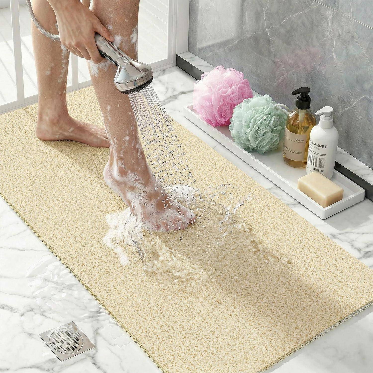 Person, die Seife von einem Fuß in einer Dusche auf einer strukturierten Badematte neben Toilettenartikeln und Badeschwämmen abspült.
