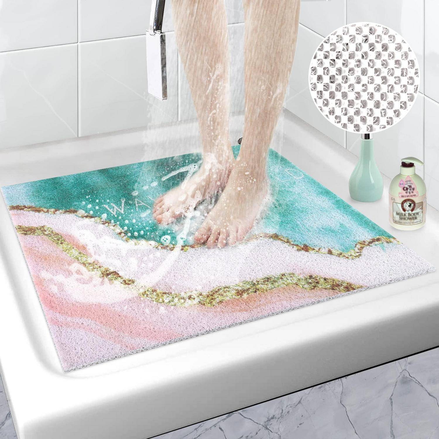 Füße, die auf einer farbenfrohen Badmatte in einer Dusche stehen, mit Wasser, das darauf fließt; eine Einfügung zeigt die strukturierte, rutschfeste Unterseite der Matte.