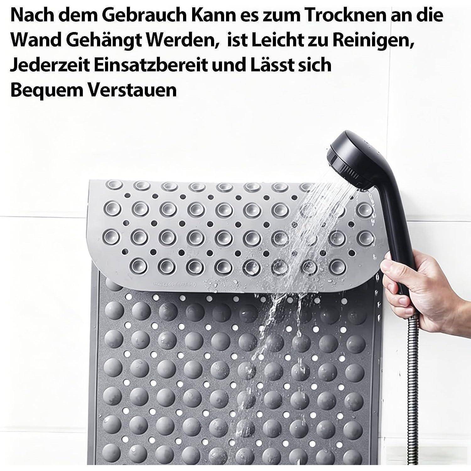 Grauefarbige, an der Wand montierte Badmatte wird mit einem Duschkopf abgespült; deutscher Text besagt, dass sie zum Trocknen aufgehängt werden kann, leicht zu reinigen ist, einsatzbereit und leicht zu lagern ist.