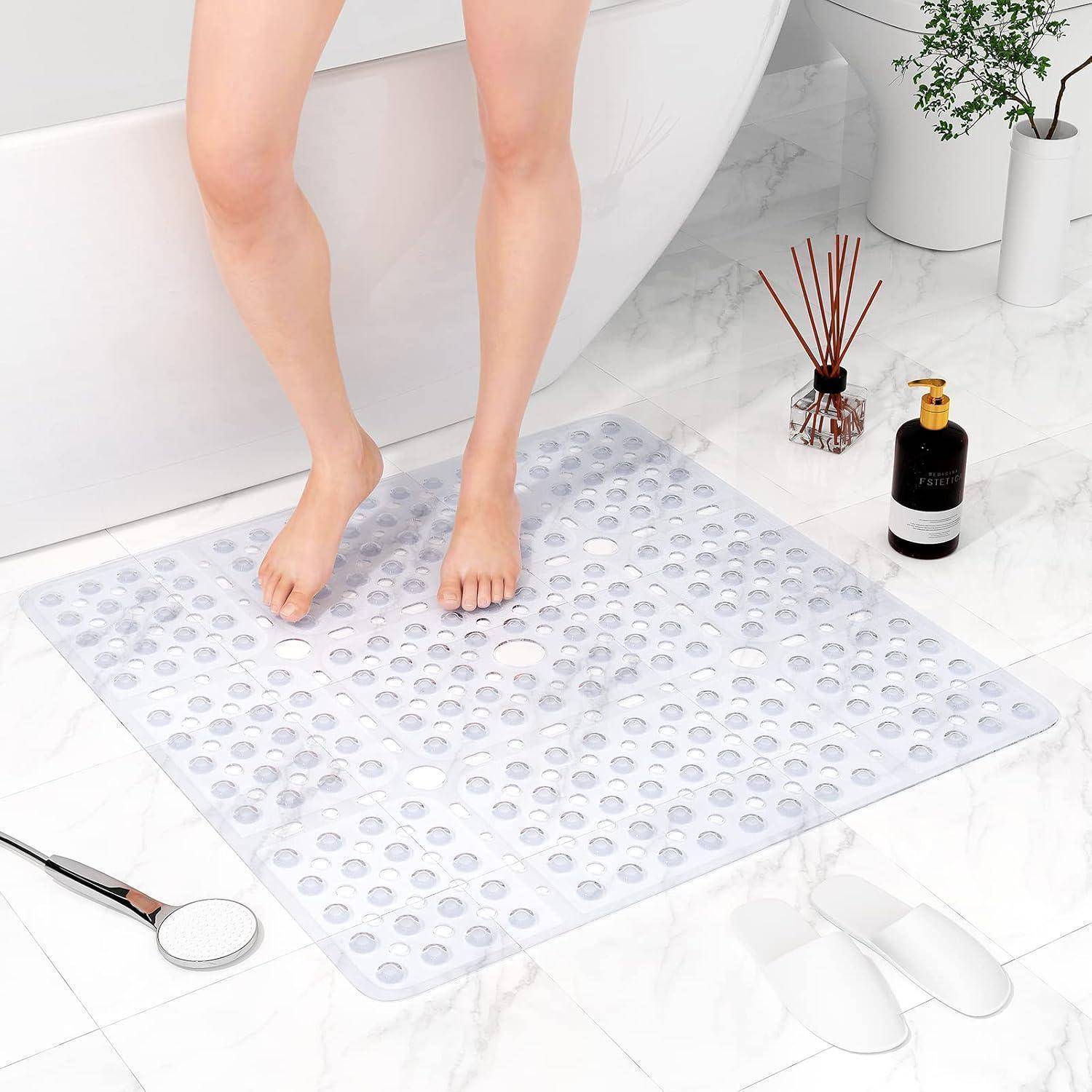 Eine Person, die barfuß auf einer transparenten Saugnapf-Badematte neben einer Badewanne in einem hellen Badezimmer steht.