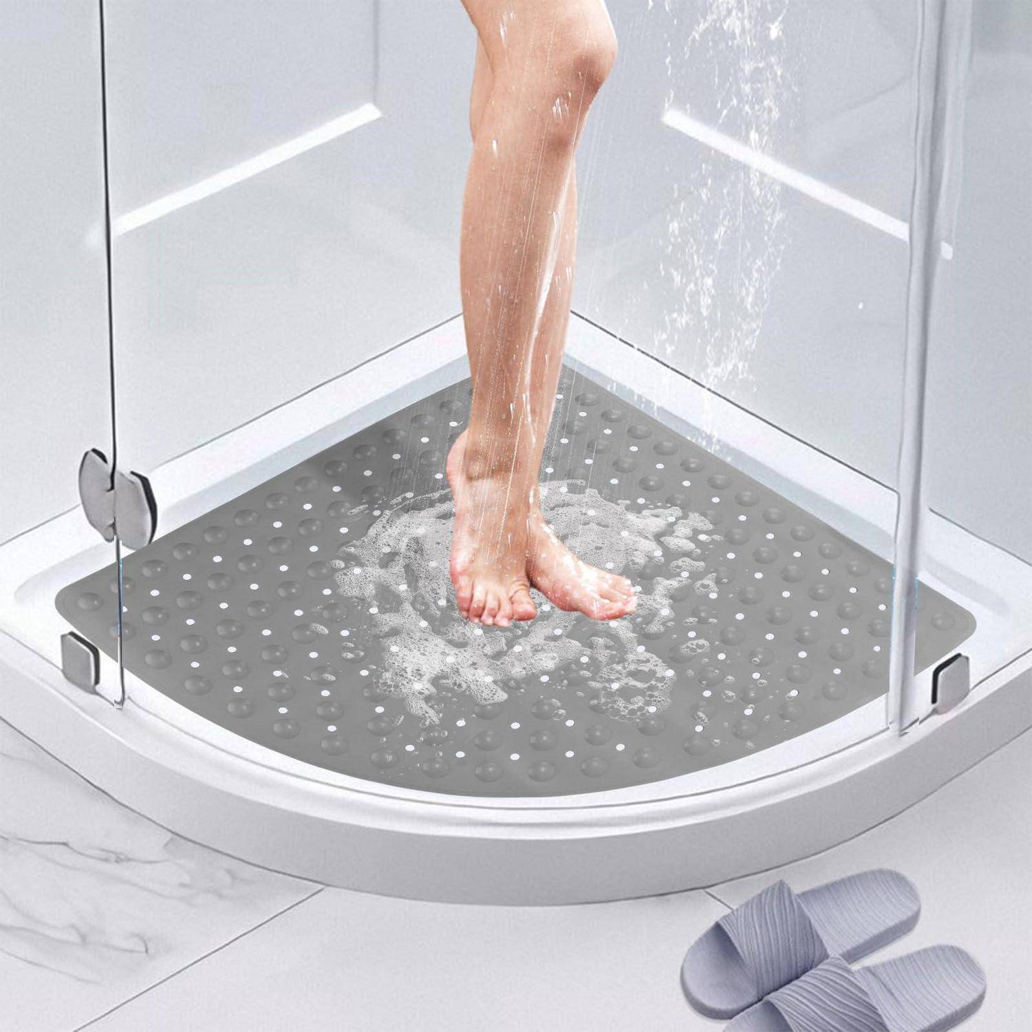 Beine und Füße in einer gläsernen Dusche, stehend auf einer grauen rutschfesten Matte mit Wasser, das auf dem Boden läuft.