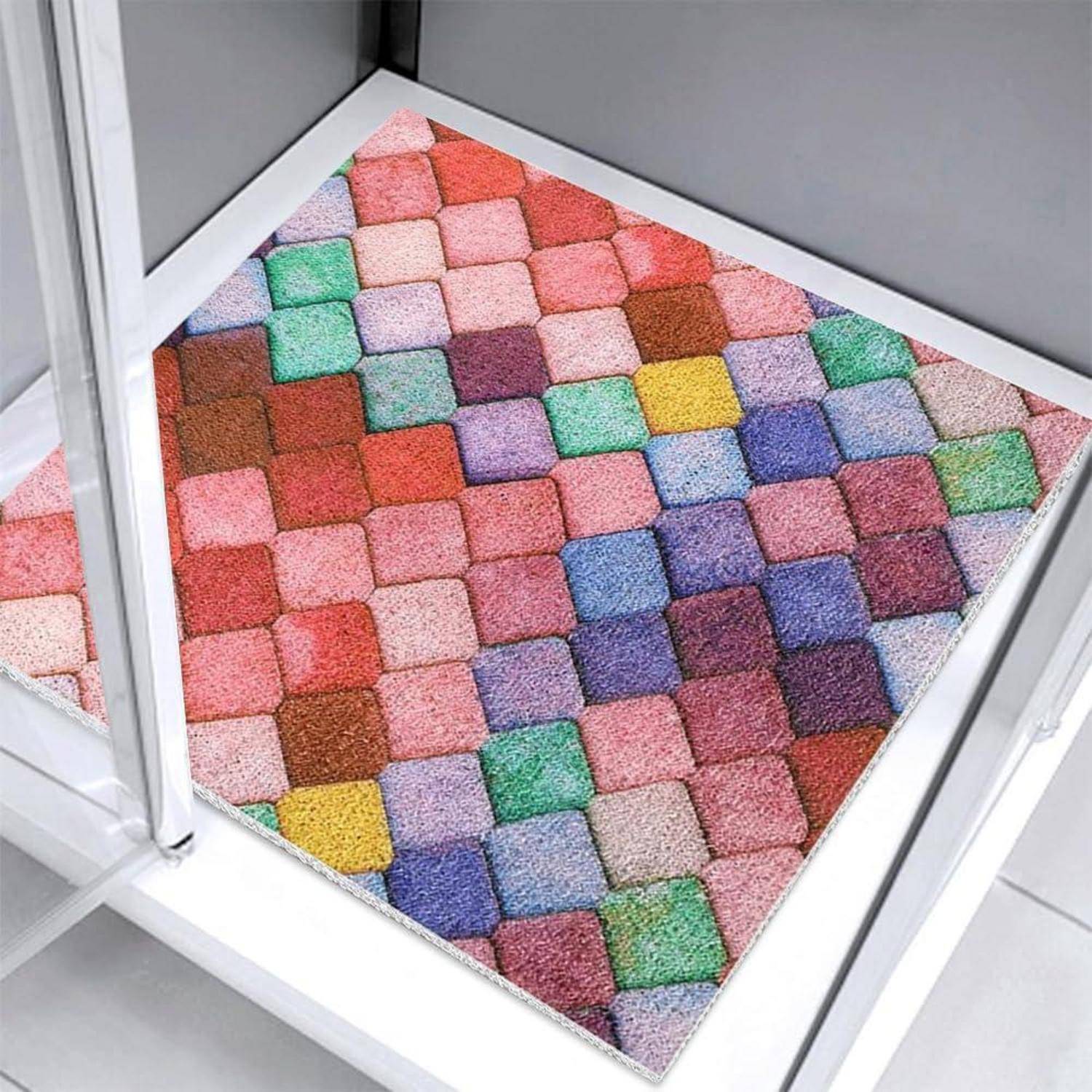 Bunter quadratischer Teppich mit einem Schachbrettmuster aus Pastell- und leuchtenden Blöcken, gezeigt in einer weiß gerahmten Ecke auf einem gekachelten Boden.