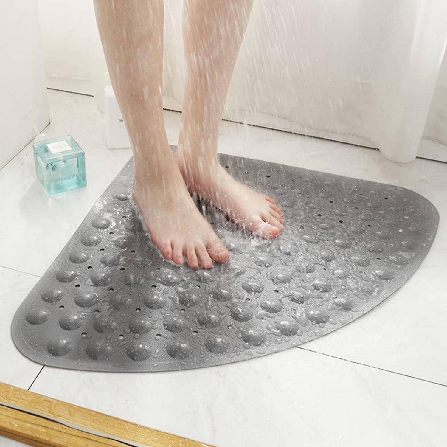 Füße stehen auf einer grauen, kieselstrukturierten Badematte auf einem nassen Badezimmerboden, mit tropfendem Wasser in der Nähe.