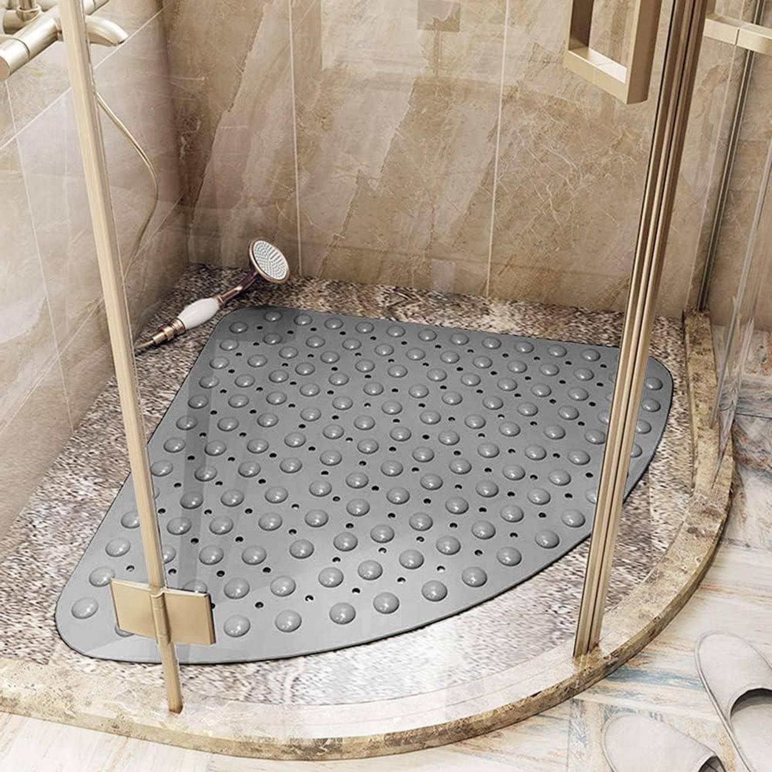 Gekrümmte graue Duscheinlage mit Saugnapfen in einer gefliesten Ecke einer Duschkabine hinter Glastüren, mit einer Handbrause in der Nähe.