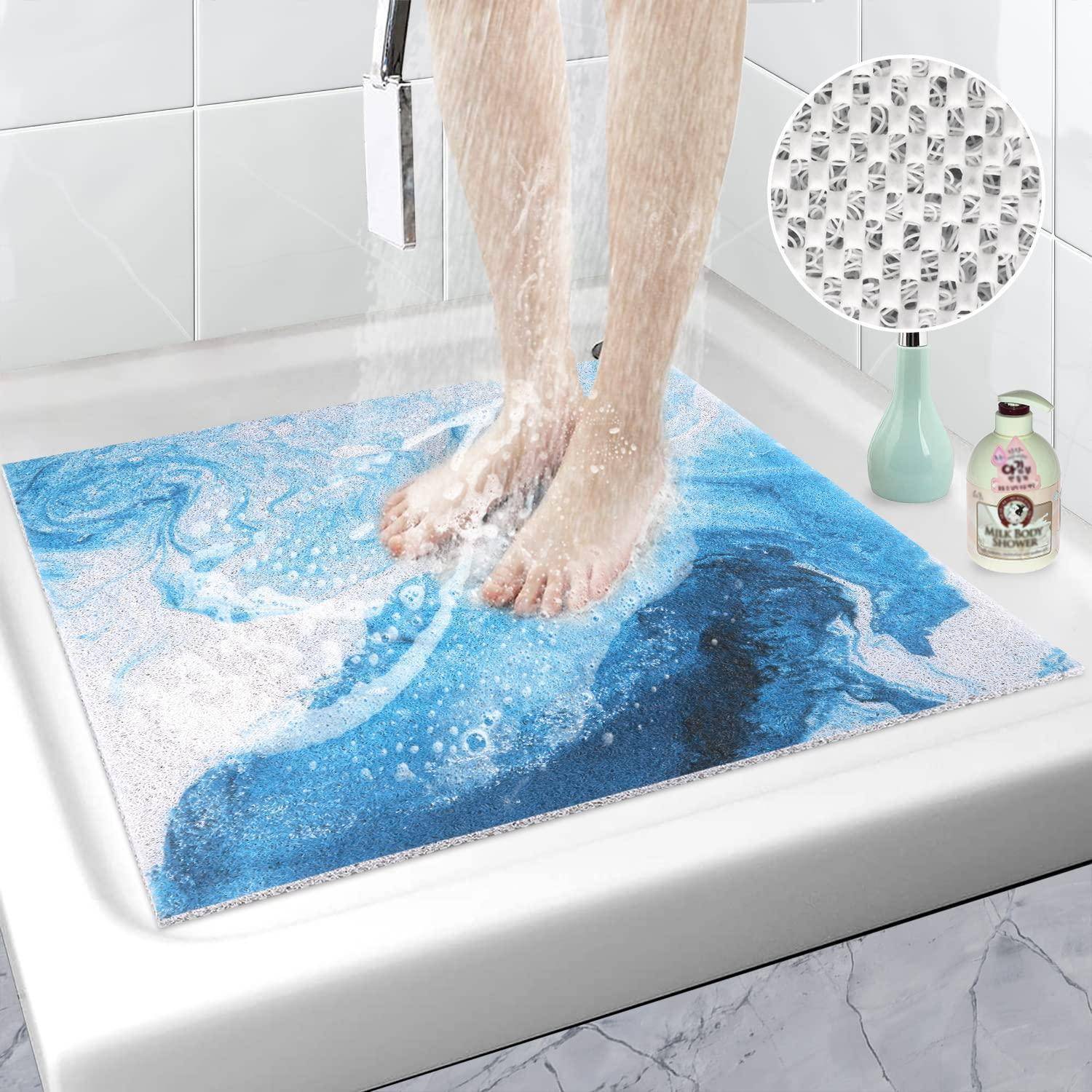 Füße, die auf einer blauen Badematte in einer Dusche stehen, mit Wasser, das durch eine Nahaufnahme mit eingefügtem Bild abfließt, das die strukturierte rutschfeste Rückseite der Matte zeigt.