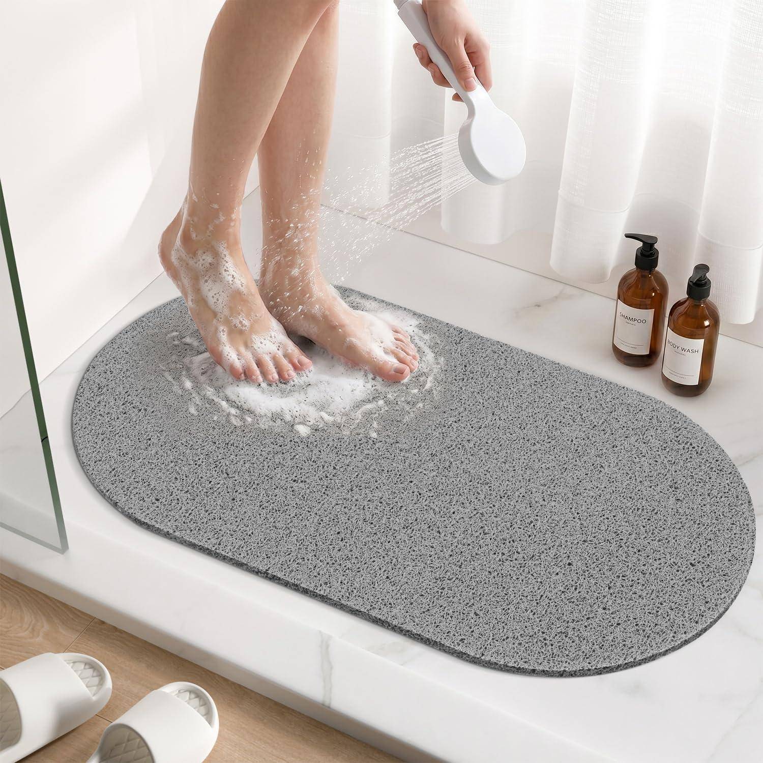 Eine Person spült seifige Füße in einer Dusche auf einer grauen Badematte neben zwei Pumpflaschen ab.