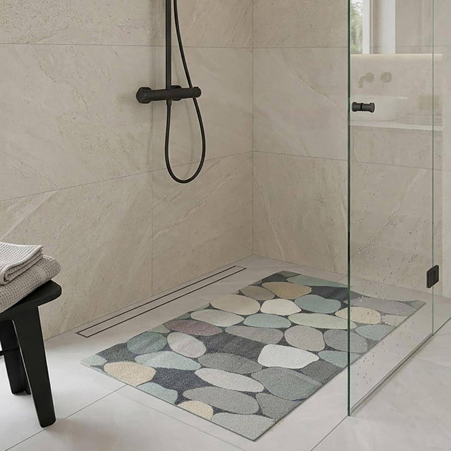 Moderne begehbare Dusche mit schwarzer Duscharmatur, Glastür und Badematte mit Kieselsteinmuster auf hellem Fliesenboden.
