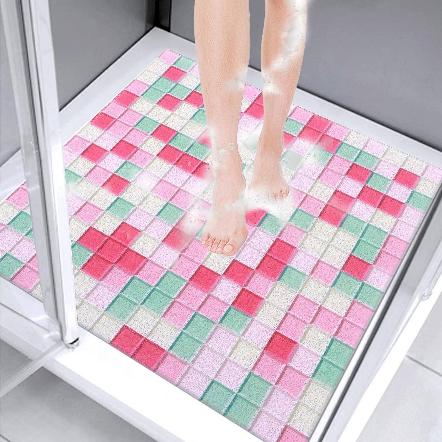 Eine Person steht in einer Dusche auf einer bunten Pastell-Mosaik-Badematte in einer gläsernen Duschkabine.