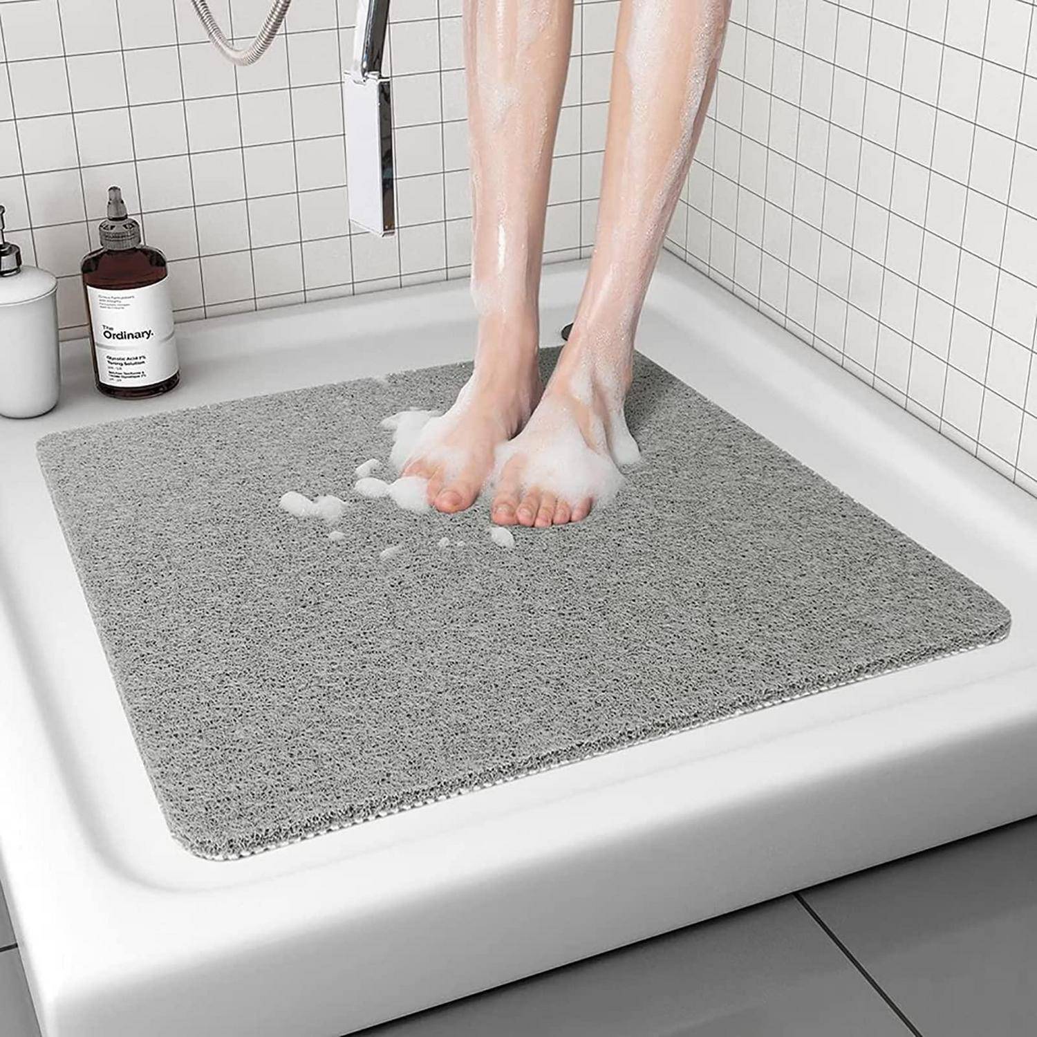 Person wäscht sich die Füße in einer Dusche, steht auf einer grauen rutschfesten Badematte, mit sichtbarem Seifenschaum.