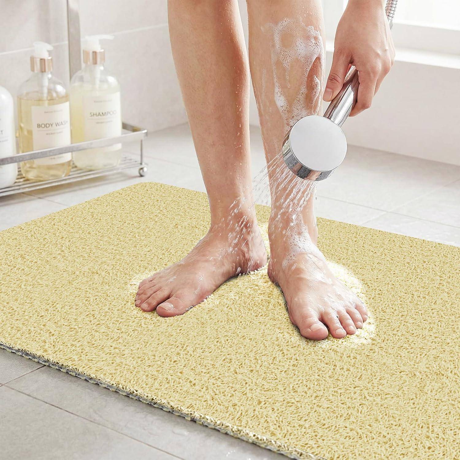 Person spült Beine und Füße mit einer Handbrause über einer strukturierten Badewannenmatte im Badezimmer ab.