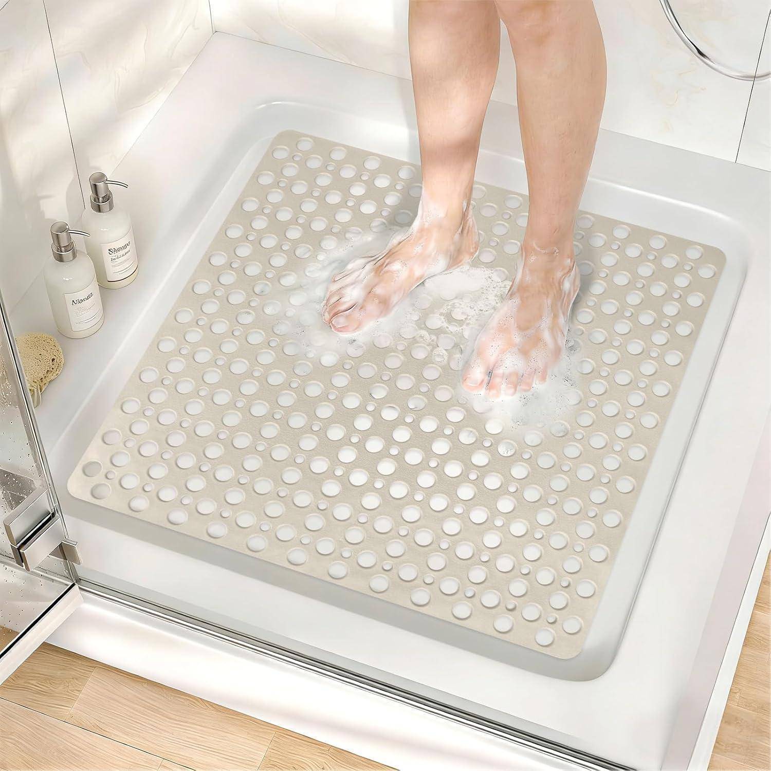 Person, die Füße in einer Dusche wäscht, während sie auf einer beigen rutschfesten Badematte mit Saugnäpfen steht.