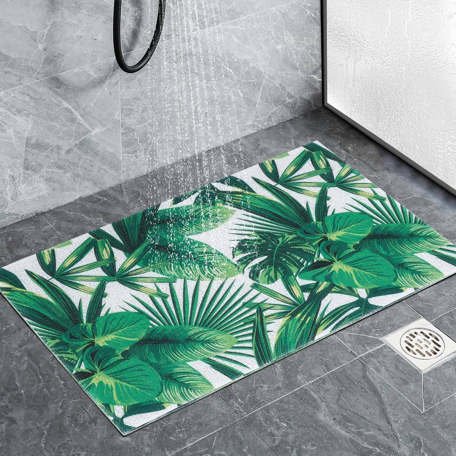 Badezimmer-Duschbereich mit einer Badematte mit tropischem Blattmuster auf grauem Fliesen unter fließendem Wasser von oben.