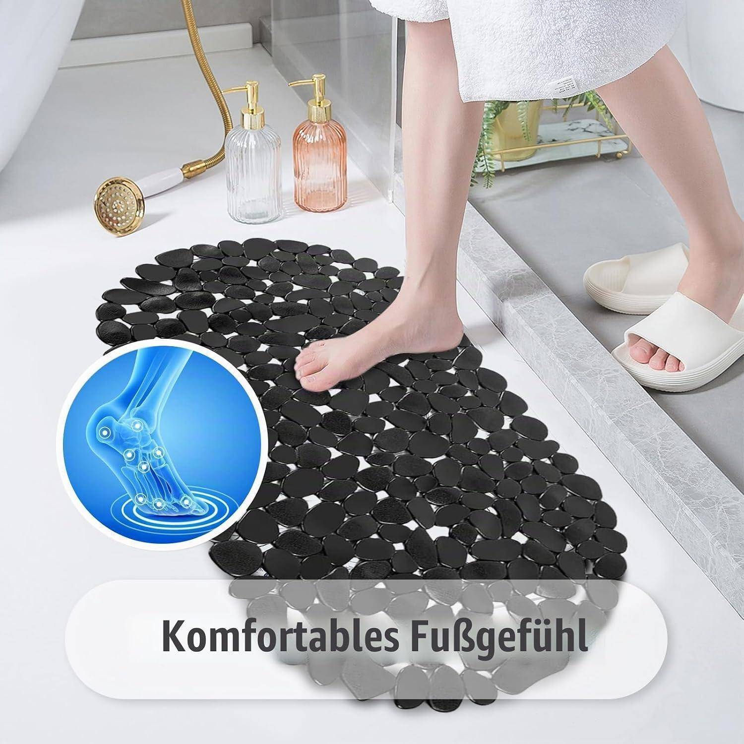 Person, der auf einer schwarzen, kieselstrukturierten Badematte im Badezimmer steht, mit deutschem Text „Komfortables Fußgefühl" und einem Fußgelenk-Komfort-Symbol.