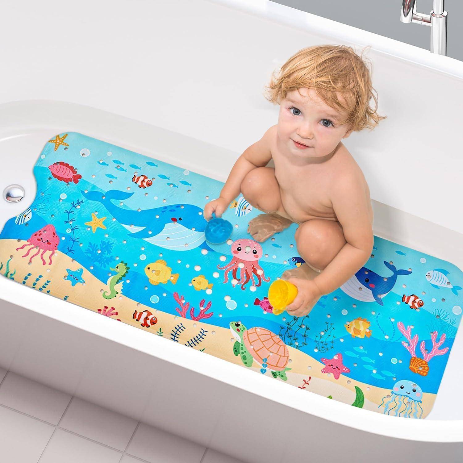 Kleinkind, das in einer weißen Badewanne sitzt und mit blauen und gelben Bechern auf einer farbenfrohen, ozeanisch gestalteten Badematte spielt.