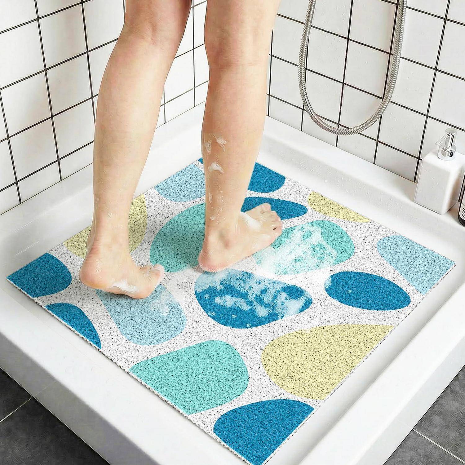 Eine Person steht auf einer farbenfrohen Badematte in einer Duschkabine, mit Wasser und Seifenschaum auf der Matte und den Füßen.