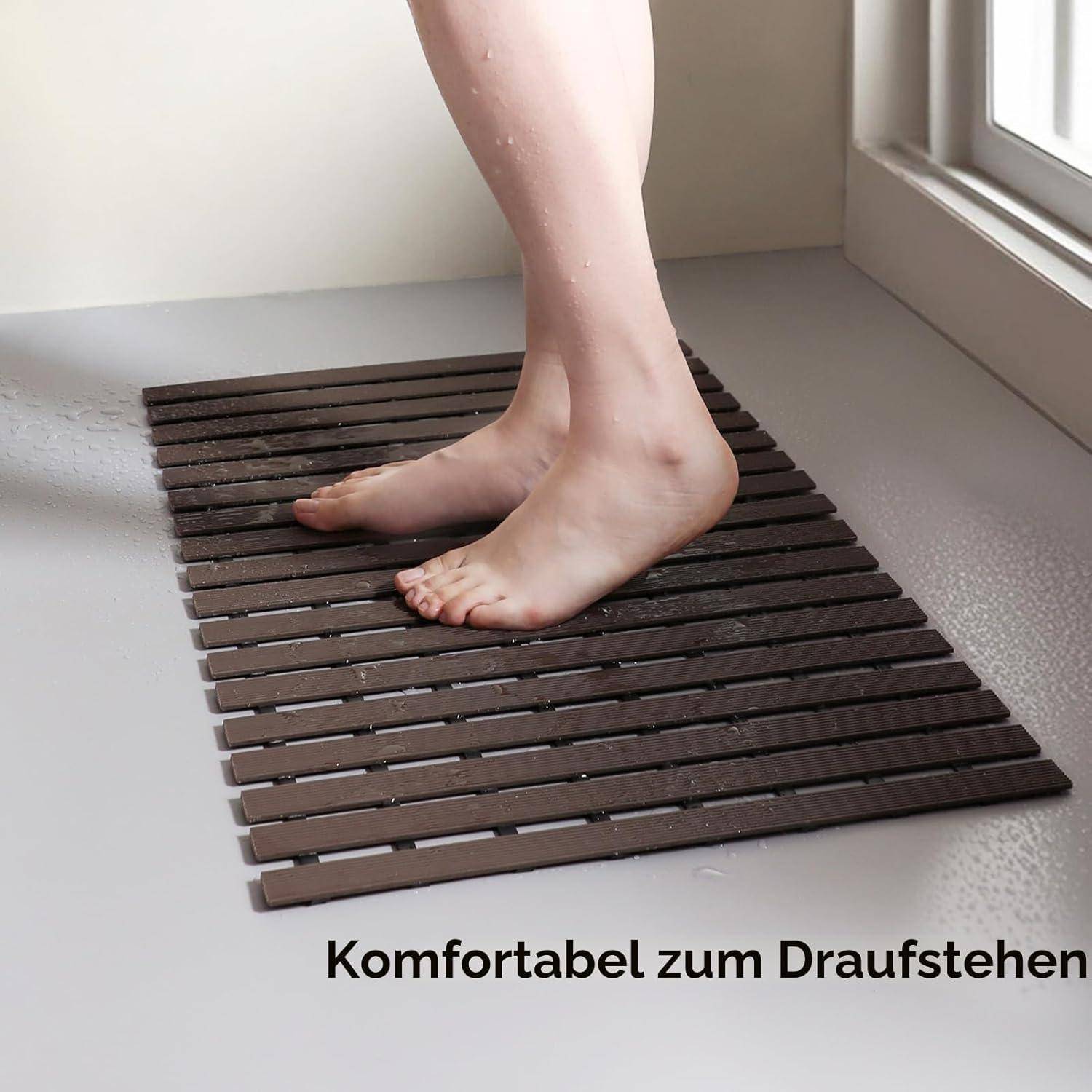 Nackte Füße, die auf einer dunklen Lamellenbadematte neben einer Dusche stehen, mit der deutschen Bildunterschrift „Komfortabel zum Draufstehen