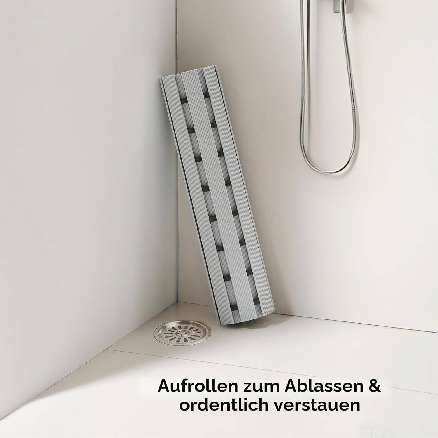 Grauer aufrollbarer Duschmat, der an einer Duschwand lehnt, mit deutschem Text „Aufrollen zum Ablassen & ordentlich verstauen