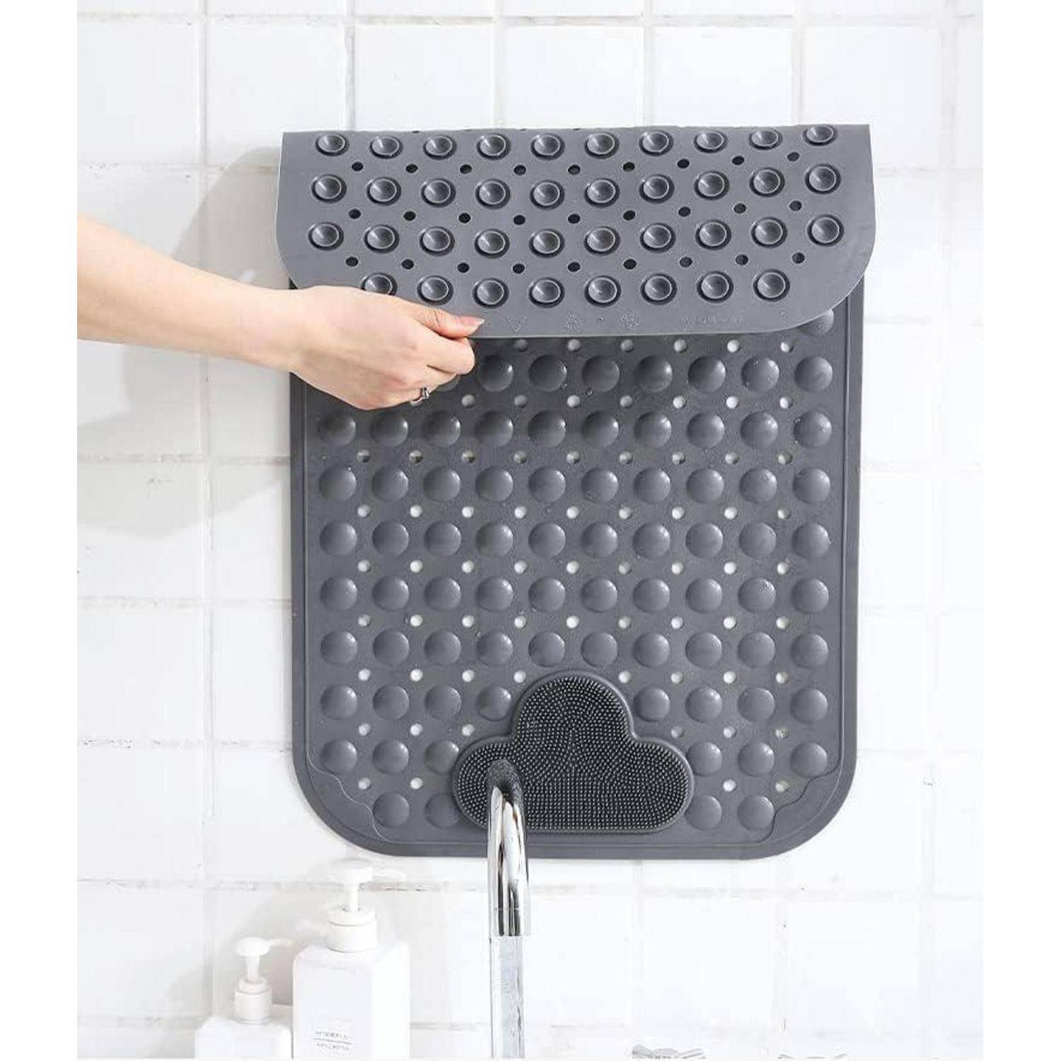 Eine Hand hebt die Klappe einer grauen, gummigen, wandmontierten Duschenmatte mit Saugnäpfen über einem Wasserhahn in einem gekachelten Badezimmer an.
