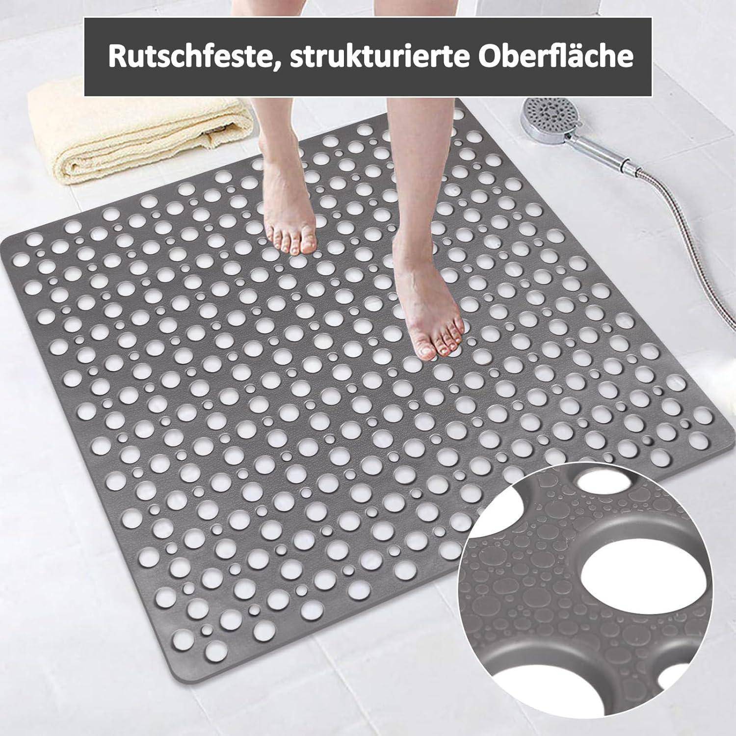 Graue perforierte rutschfeste Badmatte mit strukturierter Oberfläche, gezeigt mit Füßen und Duschschlauch; deutscher Text besagt „Rutschfeste, strukturierte Oberfläche