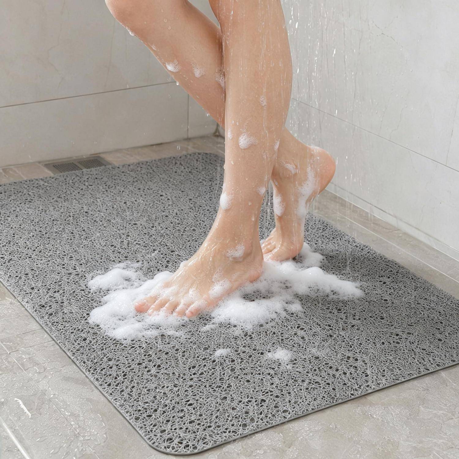 Eine Person wäscht sich die Füße in einer Dusche und steht auf einer grauen rutschfesten Matte, die mit Seifenschaum bedeckt ist.