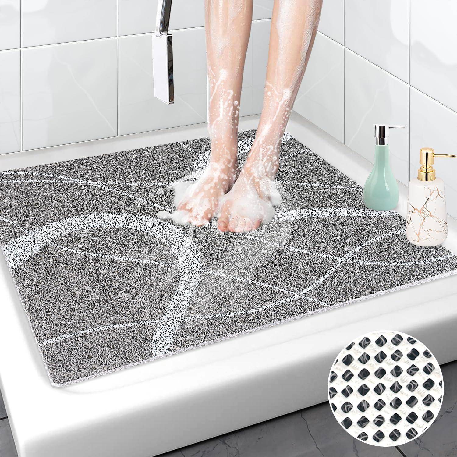 Füße, die auf einer grauen rutschfesten Badewannenmatte in einer Dusche stehen, wobei Wasser durch die strukturierte Oberfläche abfließt; die Einfügung zeigt eine Nahaufnahme des Griffmusters.