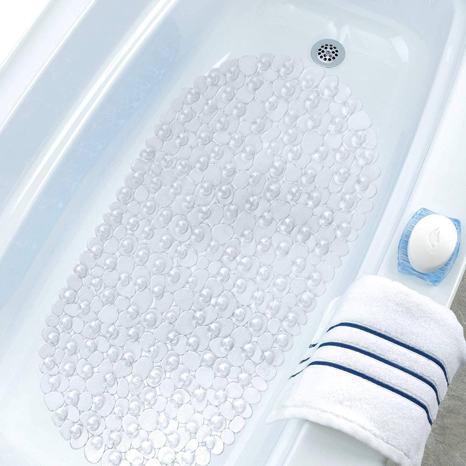 Nahaufnahme eines Badewannebodens mit einer transparenten Antirutschmatte und einer Hand, die einen Badeschwamm oder Luffa in der Nähe des Wannenrandes hält.