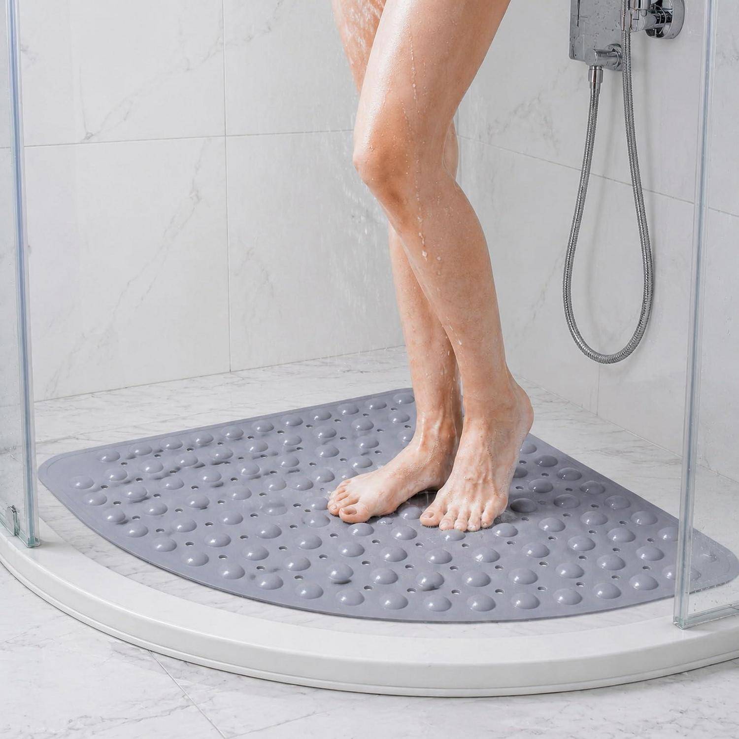 Eine Person steht unter der Dusche auf einer grauen rutschfesten Badmatte in einer gläsernen Duschkabine.