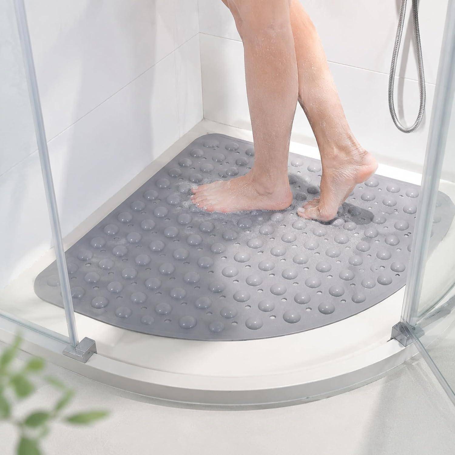 Person, die unter der Dusche auf einer grauen strukturierten rutschfesten Badmatte steht, durch eine Glastür betrachtet