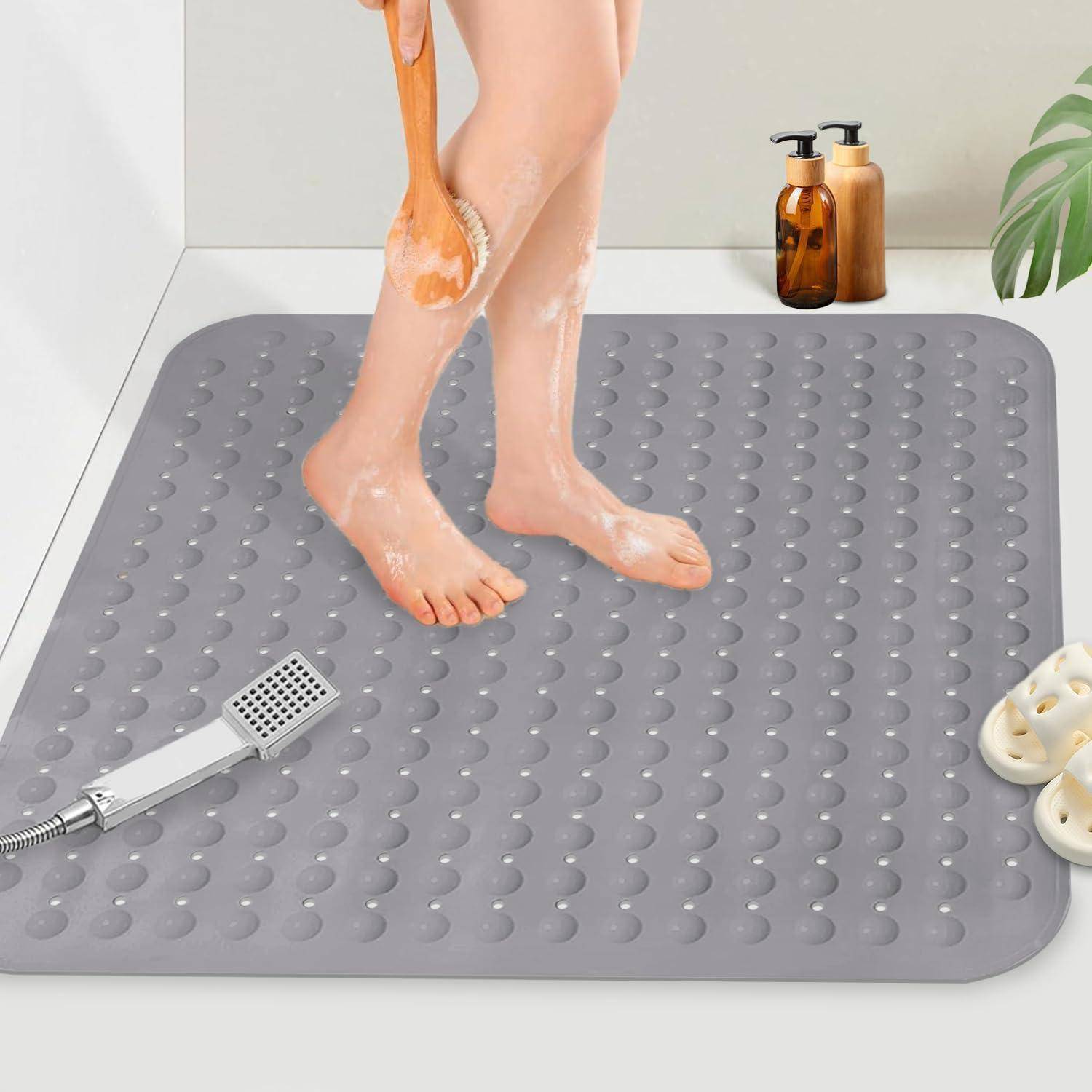 Person, der ihre Beine unter der Dusche wäscht, mit einer grauen rutschfesten Badewannenmatte, einem Handbrause-Duschkopf, Seifenflaschen und Pantoffeln in der Nähe.