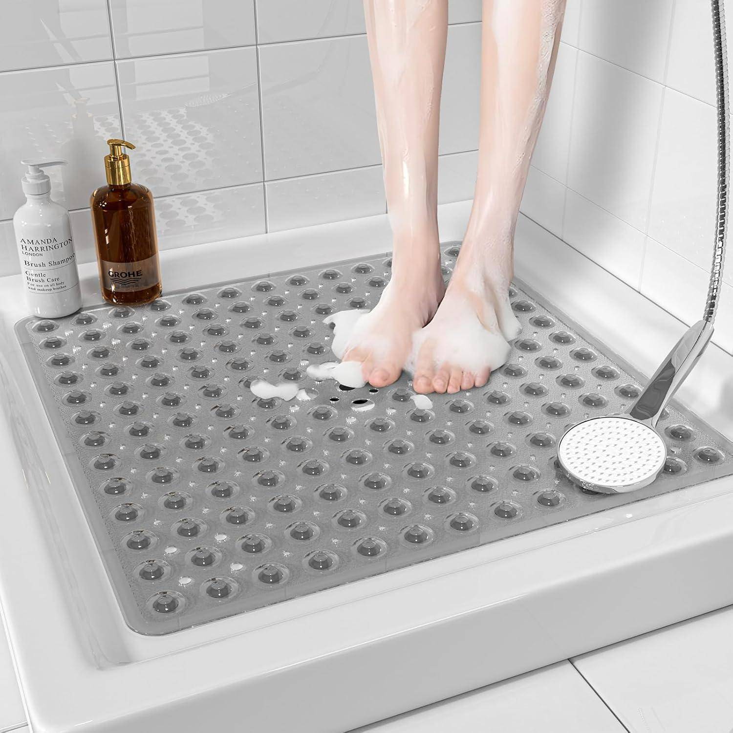 Person, der auf einer strukturierten rutschfesten Matte unter der Dusche steht, mit Seifenschaum umgeben von Badeprodukten und einer tragbaren Handbrause.