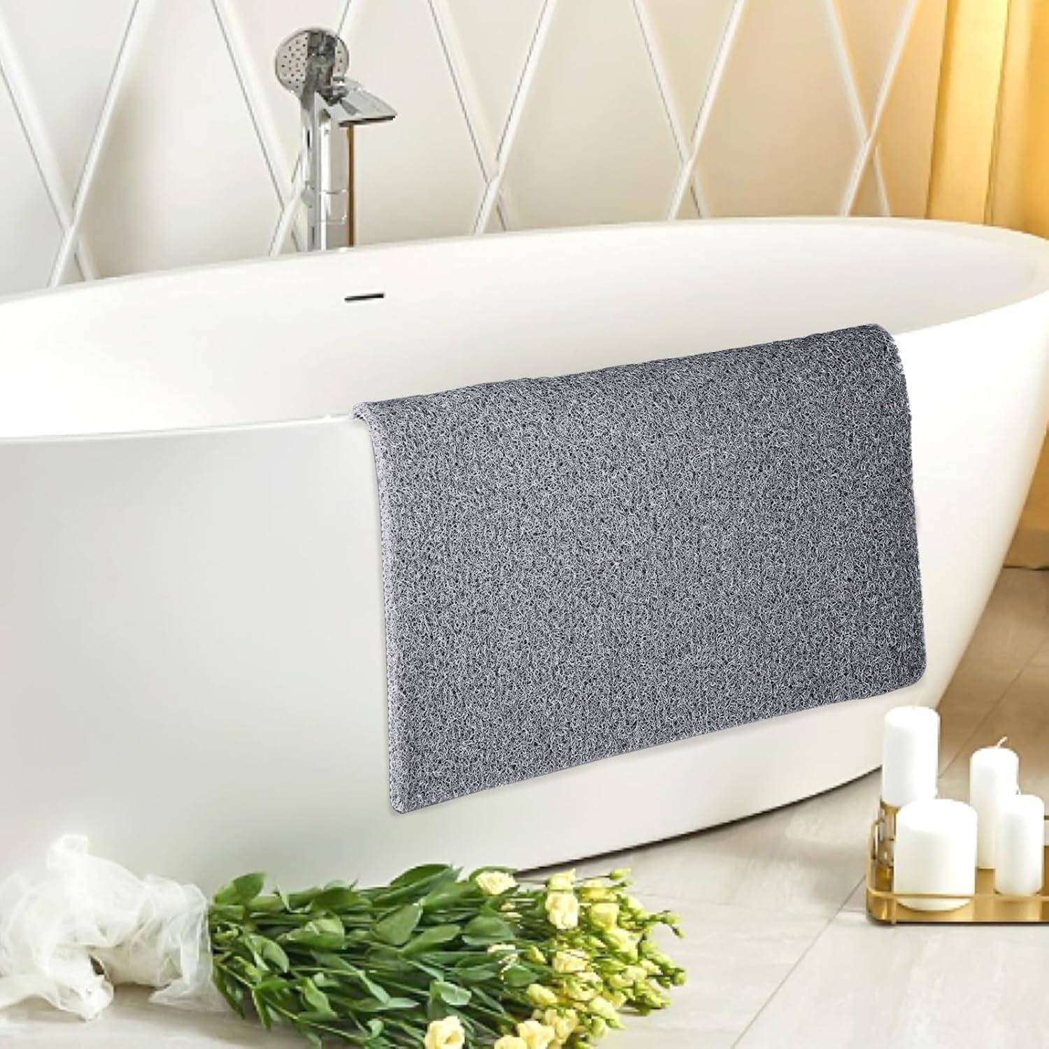 Freistehende weiße Badewanne mit grauem Badetuch über der Kante drapiert, in einem hellen modernen Badezimmer mit Blumen und Kerzen in der Nähe.