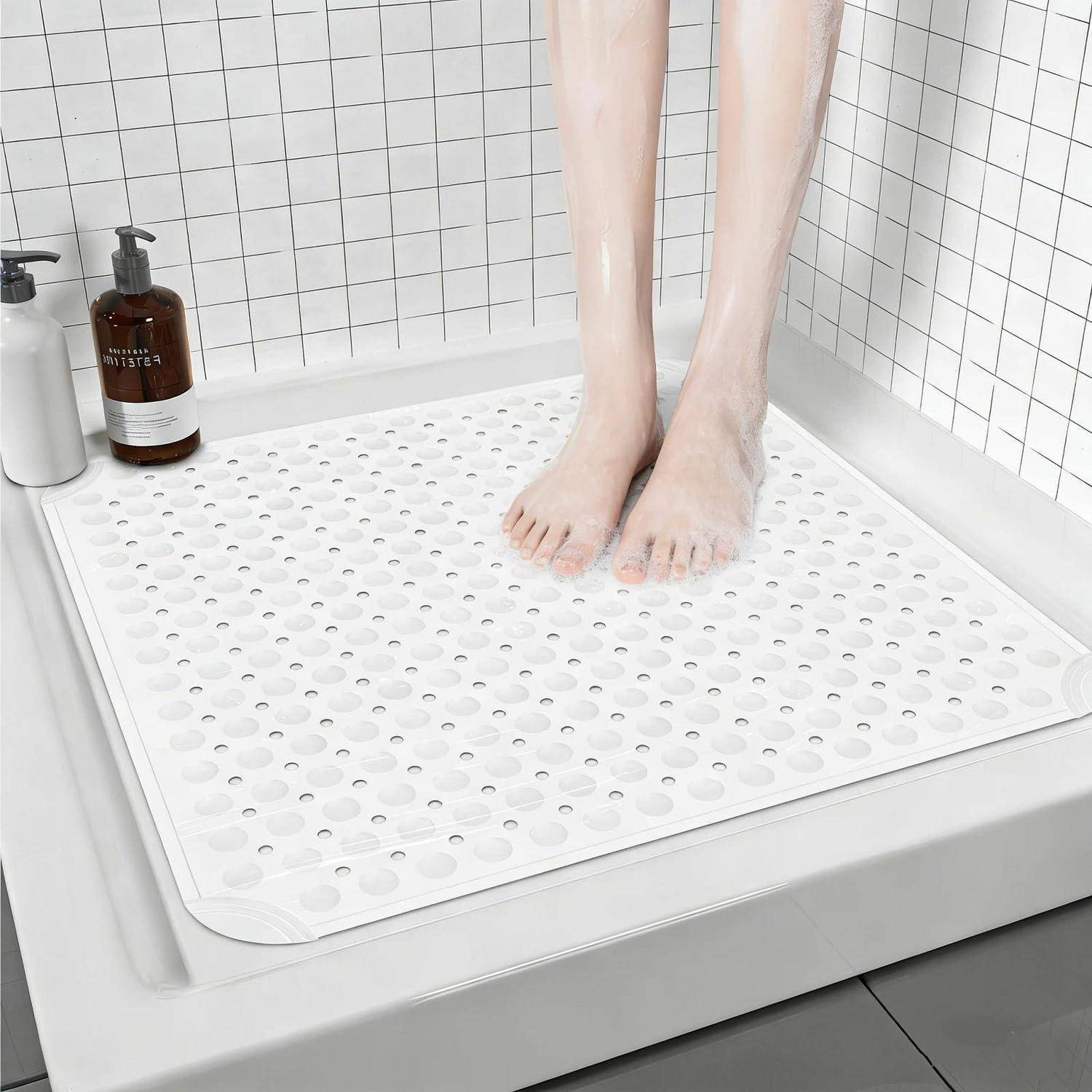Nackte Füße stehen auf einer weißen strukturierten Badematte in einer gefliesten Duschkabine, mit Flaschen auf dem Regal.