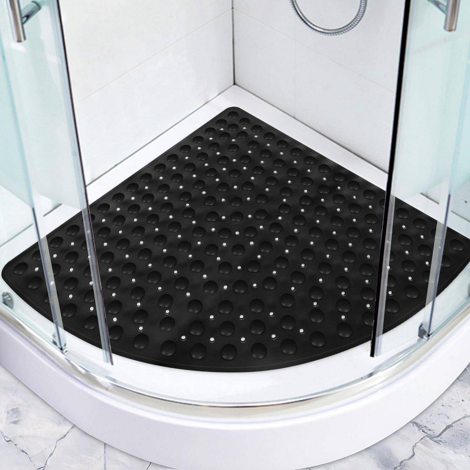 Schwarze strukturierte Gummi-Duschmatte in einer gekrümmten Glasduschkabine auf einem weißen Badezimmerboden.