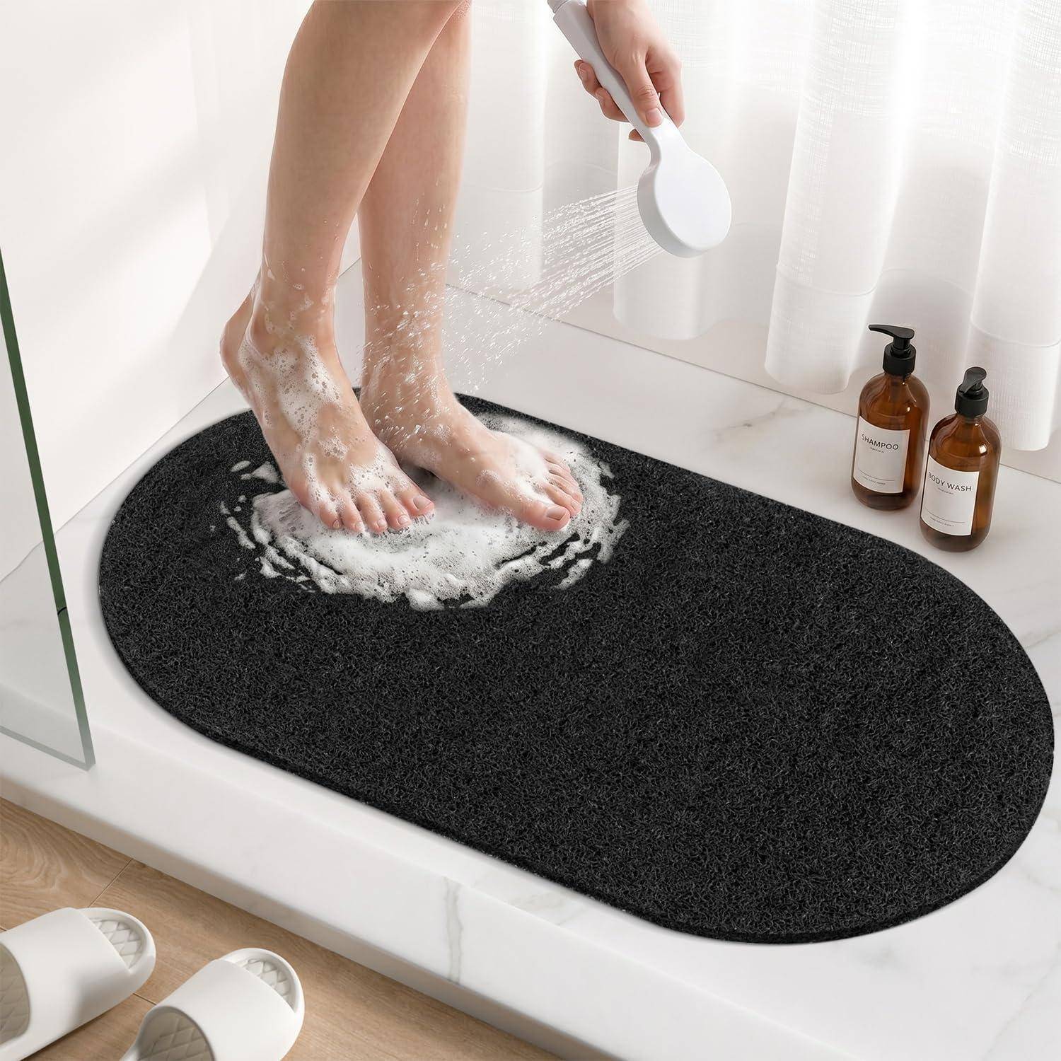 Eine Person, die Seife von ihren Füßen in einer Dusche auf einer schwarzen Badematte abspült, mit Seifenflaschen neben ihr.
