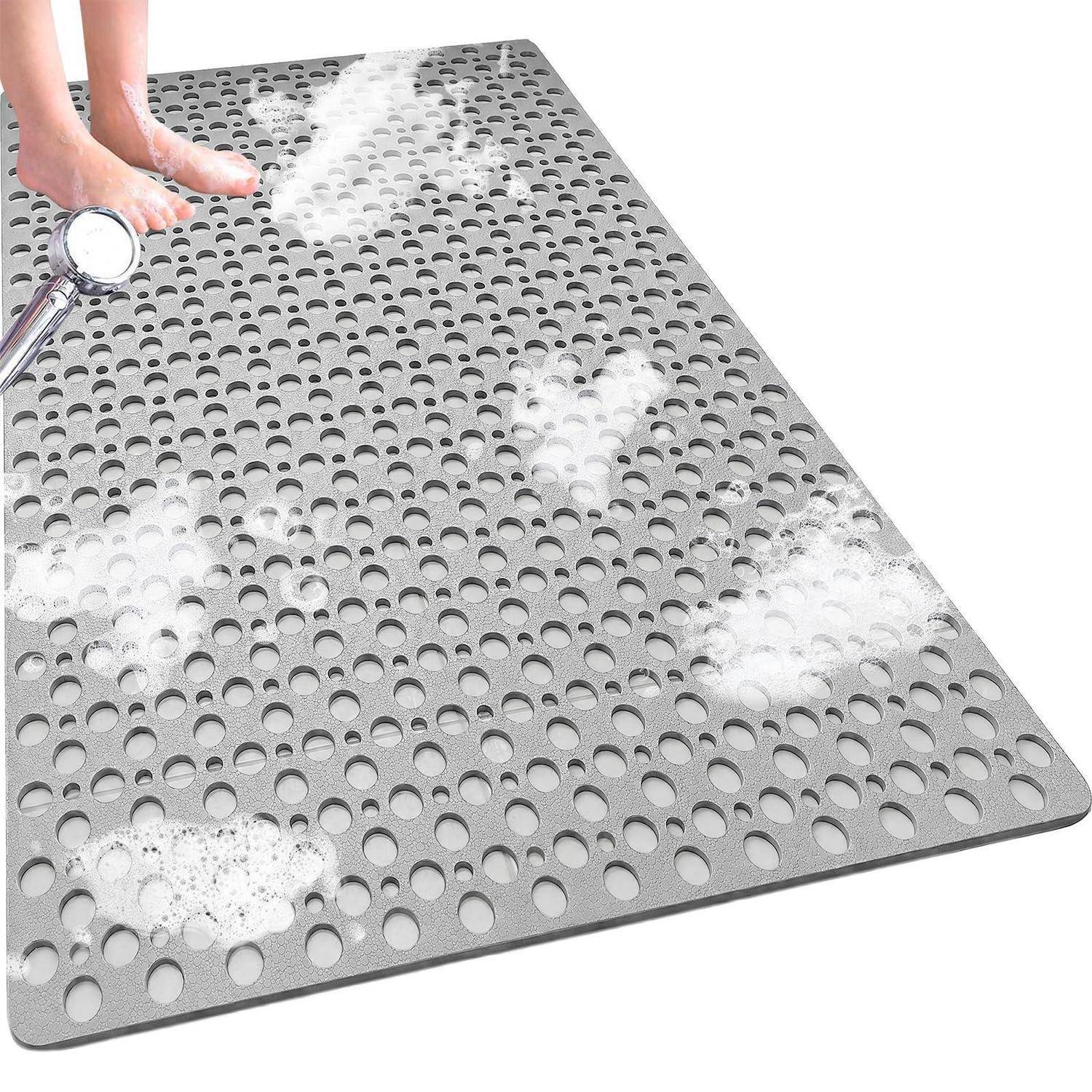 Graue Badmatte mit Perforationen aus Schaumstoff und bloßen Füßen, die eine rutschfeste Duschenmatte zeigt, die gereinigt oder abgespült wird.