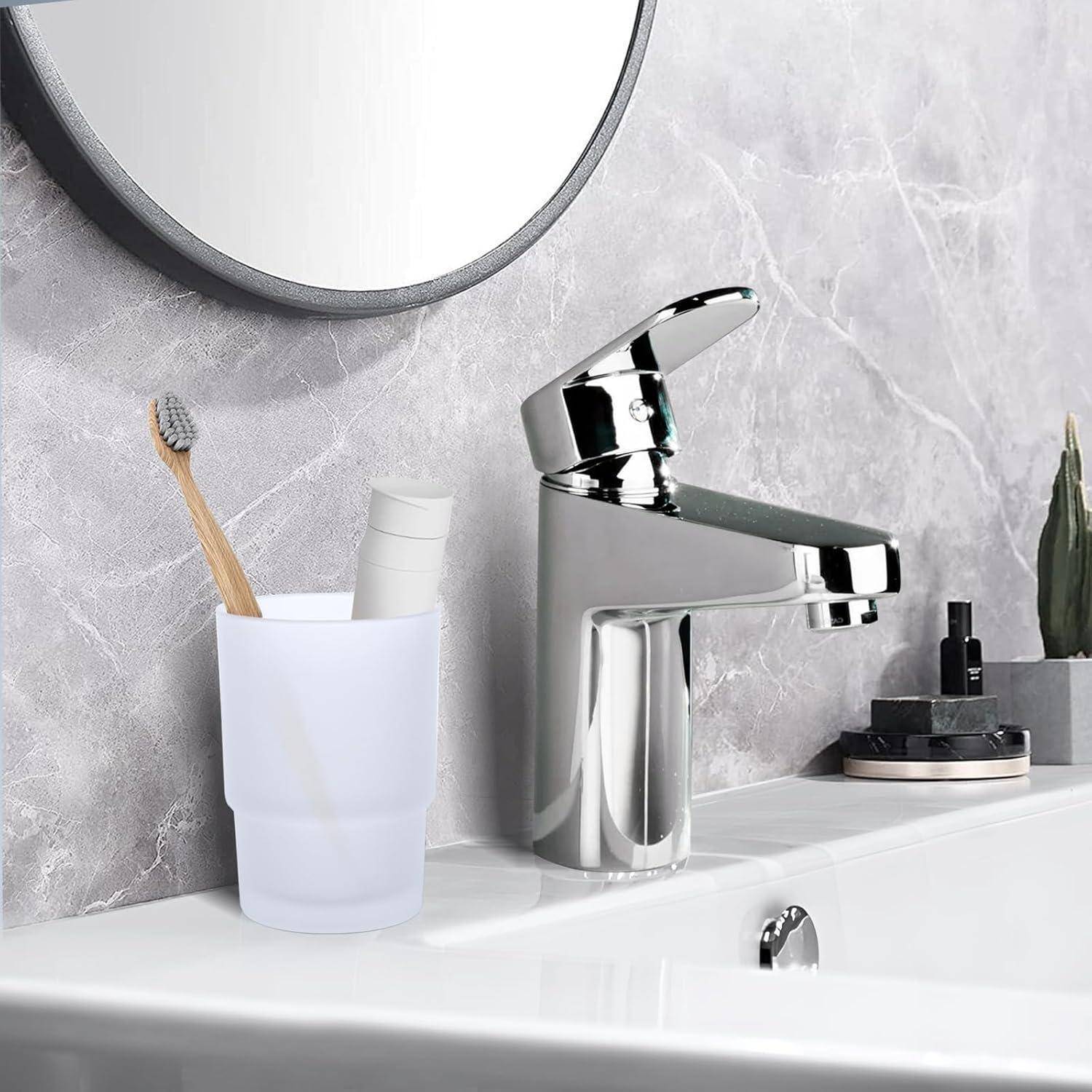 Modernes Badezimmerbecken mit Chromarmatur, Zahnbürste in weißem Becher, Spiegel darüber und kleine Dekorationsgegenstände auf einer weißen Arbeitsplatte.