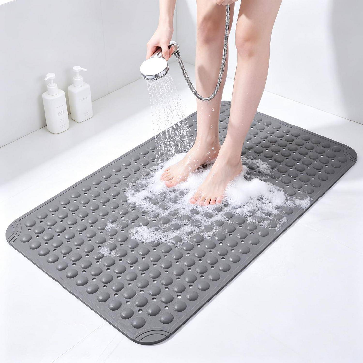 Eine Person spült ihre Füße mit einer tragbaren Dusche über einer grauen strukturierten Badmatte im Badezimmer ab.