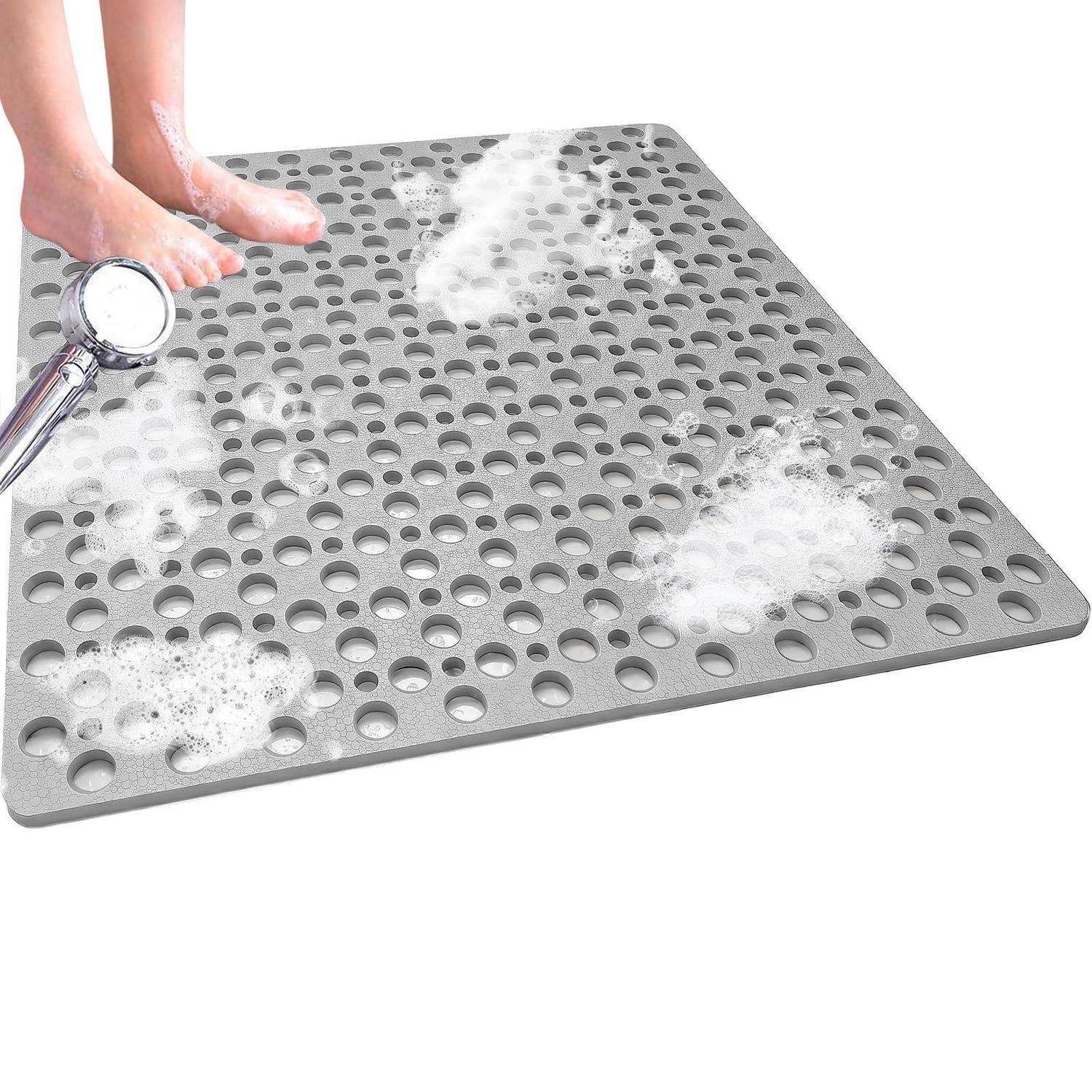 Füße spülen eine perforierte graue Duschmatte unter fließendem Wasser, mit Seifenschaum auf der Oberfläche.